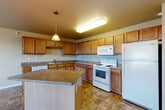 Located at 1619 Carroll St in Dickinson, North Dakota, this 2-bedroom, 1-bathroom unit offers a practical and comfortable layout across a single floor. The kitchen is a standout feature, equipped with warm honey-toned cabinetry, granite-style countertops, a central island with pendant lighting, tile flooring, and a full suite of white appliances including a refrigerator, range, microwave, and dishwasher. The open design allows for a natural flow between the kitchen and the adjacent living area, which is finished with plush carpeting and a sliding glass door that leads to a private balcony overlooking the surrounding Dickinson cityscape. The primary bedroom is generously sized, featuring a large window that brings in natural light, a wall-unit air conditioner, and baseboard heating. The second bedroom offers carpet flooring, a closet, and convenient access to the shared bathroom. The bathroom is well-appointed with a wood-toned vanity, granite-style countertops, a wide mirror, tile flooring, and a full tub-shower combination. A dedicated closet provides additional storage. Baseboard heating is present throughout the unit, ensuring comfort year-round.
