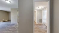 Located at 7000 Red Fox Trail in Shreveport, Louisiana, this single-floor, two-bedroom, one-bathroom home offers a practical and comfortable layout with a clean, neutral aesthetic throughout. The open-concept living room serves as the heart of the home, featuring wood-look laminate flooring, warm neutral-toned walls, and a sliding glass door dressed with vertical blinds that allows natural light to fill the space. A pass-through window connects the living area to the kitchen, enhancing the sense of openness. The kitchen is efficiently designed with white cabinetry, granite-style countertops, a sink, and black stainless appliances including a refrigerator, range, and dishwasher, all set on light wood-look flooring. Both bedrooms are carpeted for comfort, providing a softer feel underfoot. The primary bedroom offers a generous footprint and includes a window for natural light. The second bedroom features a closet with built-in shelving and hanging rod. Hallways connect the private areas of the home, adding to the functional flow. The full bathroom is finished with white tile surrounding a soaking tub and shower combo, maintaining the home's clean and consistent style. A floor-mounted HVAC vent ensures year-round climate comfort throughout the single-level layout.