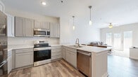 Located at 4412 Belleview Ave in Kansas City, MO, this well-designed two-bedroom, two-bathroom residence offers a thoughtfully arranged single-level floor plan. The open-concept kitchen and living area serves as the heart of the home, featuring gray shaker-style cabinetry, light quartz countertops, a full suite of stainless steel appliances including a refrigerator with ice maker, electric range with over-the-range microwave, and dishwasher. A peninsula with seating for multiple bar stools provides an ideal space for casual dining or entertaining, accented by sleek pendant lighting overhead. Wood-look plank flooring runs throughout the main living areas, lending warmth and continuity. The living room is bright and airy, with a ceiling fan, neutral walls, and French doors that invite natural light and outdoor access. Both bedrooms offer plush carpet flooring and natural light from large windows. The primary bedroom is a comfortable retreat with ample space. Each bathroom includes a walk-in shower with white tile surround and built-in corner shelving. A wall-mounted mini-split system provides efficient climate control. The overall aesthetic is clean, modern, and neutral, making for a move-in-ready space in a prime Kansas City location.