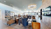 Located at 2121 West Butler Drive in Phoenix, Arizona, this elegantly designed single-floor community clubhouse offers a generous and thoughtfully curated gathering space. The entrance welcomes visitors with light hardwood flooring and framed artwork, setting the tone for the refined interiors beyond.

The expansive main lounge area is the heart of the space, featuring soaring ceilings with clerestory windows that flood the interior with natural light. Layered seating arrangements — including plush sofas, velvet accent chairs in jewel tones, and intimate conversation clusters — are anchored by a stunning tiered crystal and brass chandelier. A geometric wood-paneled feature wall with a mounted flat-screen TV adds a warm, textural focal point.

A dining and kitchen bar area seamlessly connects to the lounge, offering counter-height seating along a sleek island and café-style tables arranged in front of expansive floor-to-ceiling sliding glass doors. These doors open directly to an outdoor patio and pool area, creating a fluid indoor-outdoor living experience.

A private lounge nook, distinguished by richly painted blue-gray paneled walls, built-in shelving, and a bold mustard-yellow sectional sofa with globe wall sconces, offers a more intimate retreat within the larger space. Throughout, warm brass fixtures, curated art pieces, and a sophisticated neutral-to-bold color palette contribute to a cohesive and upscale ambiance.
