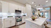 This single-floor residence showcases a thoughtfully designed open layout that blends contemporary finishes with a clean, modern aesthetic throughout. The kitchen serves as a standout centerpiece, featuring floor-to-ceiling white shaker cabinetry, a striking geometric-patterned tile backsplash, and a generous island topped with veined quartz countertops. Stainless steel appliances, including a gas range, built-in microwave, refrigerator, and dishwasher, complement the space's polished functionality. Wood-look flooring runs throughout, adding warmth and visual continuity.

The living area is bright and welcoming, anchored by French doors with transom windows above that open to a private balcony, allowing natural light to flow freely into the room. Two bedrooms provide comfortable retreats; one features a soft blue accent wall and large windows, while the other is bathed in natural light with a neutral palette. Both rooms are served by a well-appointed bathroom with dual undermount sinks, quartz countertops, white cabinetry, a large wall mirror, and light-toned tile flooring. The overall ambiance of the space is polished, airy, and cohesive.