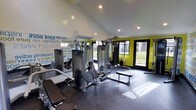This single-floor fitness center is designed to inspire and energize its users from the moment they walk in. The space features vaulted ceilings with recessed lighting that create an open, airy atmosphere, while large glass doors and expansive windows flood the interior with natural light and offer views of the surrounding greenery outdoors.

The room is anchored by a multi-station cable and weight machine system at its center, providing a comprehensive range of strength-training options. Additional equipment, including benches and free weight accessories, is thoughtfully arranged to maximize usability and traffic flow throughout the space.

The interior design is bold and motivating, with vibrant lime-green accent walls contrasting sharply against the dark rubber flooring — a practical, durable surface ideal for a high-performance workout environment. A striking typographic mural covers one wall, featuring motivational words and phrases that reinforce a culture of commitment and achievement.

A wall-mounted split air conditioning unit ensures comfortable temperatures year-round, making the space suitable for intense workouts in any season. The combination of professional equipment, energetic design elements, and thoughtful layout makes this fitness center a dynamic and functional destination for users of all fitness levels.