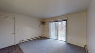 Located at 4201 W Dickman Rd in Springfield, Michigan, this single-floor unit offers a straightforward and functional layout across several well-defined living spaces. The living room is a comfortable, open area finished with plush carpet and neutral walls, featuring a wall-mounted air conditioning unit, a baseboard heater for year-round climate control, and a full-width sliding glass door dressed with vertical blinds that fills the room with natural light and provides views of the surrounding greenery outside. The kitchen is equipped with hardwood-style flooring, dark wood upper cabinetry, a gas range with an overhead exhaust hood, and a full-size refrigerator, offering a practical setup for everyday cooking. The bedrooms are carpeted and bright, with clean white walls and baseboard heating. One bedroom features a built-in closet with louvered bifold doors, an overhead shelf, and a hanging rod, providing convenient storage. The bathroom includes a full tub and shower combination with white tile surround, chrome fixtures, and hardwood-style flooring, maintaining a clean and functional aesthetic. Throughout, the unit presents a consistent, neutral palette with textured ceilings, creating a modest and move-in ready living environment.