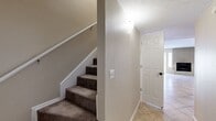 This two-story residence offers a well-organized layout with living space evenly divided between its two floors. The main level features large-format ceramic tile flooring throughout the entry hallway, living room, and kitchen. The entry hallway, accessible via a paneled front door, connects directly to the carpeted staircase, which is lined with a white handrail and textured walls. The living room is a generously proportioned open space equipped with a ceiling fan and neutral-toned walls, providing a versatile area for various arrangements. The kitchen is outfitted with dark espresso cabinetry, ample counter space in an L-shaped configuration, tile flooring, and a white appliance suite including a range and refrigerator. The upper floor hosts both bedrooms, each featuring plush carpeting, ceiling fans with light fixtures, and windows fitted with blinds. The spacious primary bedroom offers a comfortable retreat. Both bathrooms include full tub-shower combinations with floor-to-ceiling stone-look tile surrounds, mosaic accent borders, tile flooring, and vanities with matching countertops. Each bedroom is accompanied by a dedicated closet, enhancing storage throughout the home.