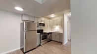 This single-floor unit offers a clean, contemporary design with a neutral color palette and durable wood-look flooring throughout the main living areas. The kitchen is a standout feature, equipped with stainless steel appliances including a full-size refrigerator, electric range, over-the-range microwave, and dishwasher. Gray shaker-style cabinetry with brushed metal hardware lines both the upper and lower sections, complemented by light-toned countertops and a double-basin sink. Ample cabinet storage makes this an efficient and functional cooking space. The open living and dining area is bright and versatile, featuring wood-look flooring and a sliding glass door that provides access to an outdoor space while bringing in natural light. An adjacent secondary space with the same flooring offers additional flexibility for a dining setup or workspace. The bedroom features plush carpeting, a large window that allows generous natural light, and neutral walls that create a calm, restful atmosphere. The bathroom is finished with a gray vanity cabinet, white countertop, single-basin sink, and a combined tub and shower enclosure, maintaining the cohesive modern aesthetic found throughout the unit.