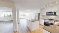 Located on the 7th floor at Halifax Street in Burnaby, BC, this one-bedroom, one-bathroom unit offers a clean, modern interior with a well-considered layout. Light-toned laminate flooring runs throughout, complementing the bright white walls and creating a cohesive, airy aesthetic.

The open-concept kitchen and living area forms the heart of the unit. The kitchen is equipped with stainless steel appliances including a refrigerator, range, and microwave, set against white shaker-style cabinetry and a subway tile backsplash. Dark quartz countertops provide a striking contrast, and a compact island adds additional prep and storage space. The living area benefits from large floor-to-ceiling windows that admit generous natural light and frame views of surrounding treetops and the Burnaby skyline.

The bedroom is a well-proportioned, quiet retreat featuring oversized windows with leafy green views, light hardwood-style flooring, and a glass-panel sliding door that connects to a private balcony area, enhancing the sense of openness.

The bathroom is finished to a high standard, with a quartz vanity countertop, undermount sink, chrome fixtures, elegant vanity lighting, a large mirror, and subway-tiled shower walls. The overall ambiance throughout the unit is bright, clean, and contemporary.