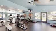 Located at 1501 Cobble Creek Circle in Rocklin, California, this fitness center offers a well-equipped workout space designed to support a variety of exercise routines. The room features vaulted ceilings that lend an open, airy feel, complemented by soft blue-gray walls that create a calm and focused atmosphere. Durable rubber flooring covers the entire space, providing a safe and practical surface for exercise. A ceiling fan overhead ensures comfortable air circulation during workouts.

The facility is outfitted with a comprehensive selection of cardio machines, including treadmills, an elliptical cross-trainer, a stationary upright bike, and a recumbent stepper. A multi-station cable machine and a rack of dumbbells with an adjustable weight bench accommodate strength training needs. A wall-mounted flat-screen television adds entertainment during workouts.

Full-length mirrors line one wall, visually expanding the space and allowing users to monitor their form. Multiple windows fitted with blinds allow generous natural light to fill the room while offering views of the surrounding outdoor areas, including a glimpse of a pool area. A glass-paneled door provides direct outdoor access, further enhancing the bright, welcoming environment of this practical and functional fitness facility.