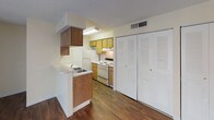 This single-floor unit offers a clean, functional layout designed to maximize comfort and usability throughout. The living area is an open, welcoming space finished with rich, dark hardwood-style flooring that flows consistently throughout the unit. A large sliding glass door dressed with vertical blinds fills the room with natural light and provides outdoor access. Neutral, warm-toned walls complement the flooring and create a bright, airy ambiance.

The kitchen is efficiently laid out with a peninsula-style counter featuring a double sink, warm wood cabinetry, a white electric range with overhead ventilation, a refrigerator, and ample upper and lower cabinet storage. A textured popcorn ceiling is present throughout the unit.

The bedroom is generously sized and features an impressive amount of built-in closet space, with multiple louvered bifold closet doors providing substantial storage. An attached bathroom is accessible from the bedroom and includes a full tub and shower combo with clean white tile surround, a vanity, and a toilet.

The bathroom is bright and straightforward in design, with a chrome towel bar and tiled shower walls. The unit's consistent flooring, abundant natural light, and practical layout make it a highly functional and comfortable single-floor living space.