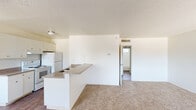 This single-floor unit offers a functional and straightforward layout designed for comfortable everyday living. The open-concept kitchen and living area form the heart of the space, where a peninsula countertop with granite-style laminate surfaces separates the kitchen from the carpeted living room. The kitchen is well-equipped with white cabinetry, a coil-element electric range, a full-size refrigerator, an under-cabinet range hood, and a double-basin sink — all finished in white for a clean, cohesive look. Wood-style flooring runs through the kitchen and entryway, transitioning to neutral wall-to-wall carpeting in the living and bedroom areas. The living room is generously sized, featuring multiple windows that allow natural light to fill the room, along with a textured popcorn ceiling consistent throughout the unit. The bedroom offers a quiet, carpeted retreat with a window providing natural light and ventilation. The bathroom includes a white vanity with an integrated sink, a framed mirror with overhead lighting, and a full-size soaking tub with a showerhead and chrome fixtures, accompanied by a frosted window for privacy. The unit's clean white walls and neutral finishes create a bright, move-in ready environment.