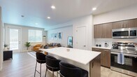 This well-designed 2-bedroom, 1-bathroom unit offers a thoughtful layout that maximizes functionality across a single floor. The open-concept kitchen and living area serves as the heart of the home, anchored by a generous white-topped island with bar seating — ideal for casual dining or entertaining. The kitchen is equipped with stainless steel appliances, including a refrigerator, range, microwave, and dishwasher, complemented by warm wood-toned cabinetry and clean white countertops. Light wood-style flooring runs throughout the unit, creating a cohesive and contemporary feel. The living area is bright and welcoming, featuring a glass-panel exterior door and a large window that invites natural light. A distinct entryway with a console and round mirror provides a stylish transition into the main living space. Both bedrooms are comfortably sized, with the primary bedroom offering a large window dressed with blinds and sheer curtains for adjustable light control. The shared full bathroom includes a tub-shower combination with clean white tile surround. Recessed lighting throughout adds a modern, polished finish to the overall aesthetic of this efficiently designed and well-appointed unit.