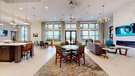 Located at 6386 Transit Rd in Depew, NY, this contemporary amenity center is thoughtfully designed to provide a refined, resort-style experience. The expansive clubroom serves as the heart of the space, boasting soaring double-height ceilings, large black-framed windows that flood the interior with natural light, and floor-to-ceiling drapes. Comfortable seating arrangements, round dining tables, and a billiards table create a versatile environment suited for both socializing and relaxation. Light wood-style flooring and layered area rugs add warmth throughout. A well-appointed community kitchen features dark wood cabinetry, granite countertops, stainless steel appliances, and a striking buffalo mural that adds a local artistic touch. The fitness facilities are comprehensive and modern, including a cardio room equipped with treadmills, ellipticals, and cable machines alongside floor-to-ceiling mirrors, as well as a dedicated spin studio with cycling bikes, a wall-mounted TV, and expansive windows overlooking the outdoors. The entrance lobby features double-height ceilings, bold abstract artwork, and elegant wingback seating, establishing a sophisticated first impression. Throughout the space, a cohesive neutral palette, curated artwork, and contemporary fixtures create a polished and welcoming atmosphere.