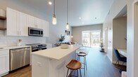 This well-designed single-floor residence showcases a thoughtful open-concept layout that seamlessly connects the kitchen, dining, and living areas. The kitchen is a standout feature, boasting crisp white shaker cabinetry, a classic subway tile backsplash, stainless steel appliances including a refrigerator, range, microwave, and dishwasher, and warm wood open shelving. A generous island with a sleek white countertop provides bar seating and serves as the centerpiece of the space. Pendant lighting overhead adds a modern, polished touch. The living area is bright and welcoming, with hardwood-style flooring flowing throughout and a sliding glass door that opens to a private balcony, bringing in abundant natural light and outdoor views. The bedroom is a serene retreat featuring large windows that continue the connection to the outdoors, plush carpeting, and access to a spacious walk-in closet with ample shelving and hanging space. The full bathroom is finished with subway tile in the tub/shower surround, a white vanity, and hardwood-style flooring, maintaining the clean, contemporary aesthetic found throughout the home. A dedicated laundry area with an in-unit washer and dryer adds everyday convenience to this modern, cohesive living space.