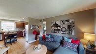 This single-floor, two-bedroom, one-bathroom residence at The District in University City, Missouri offers a thoughtfully designed layout that maximizes its well-proportioned footprint. The living room serves as the central gathering space, featuring hardwood-style flooring, a textured ceiling, and multiple windows dressed with rich burgundy curtains that allow for ample natural light and outdoor views of greenery. The open sightline connects the living area to the kitchen, which is outfitted with rich dark wood cabinetry, granite-style countertops, a stainless steel dishwasher, and a double-basin sink beneath a window overlooking the exterior. A freestanding kitchen island provides additional prep and dining space. The two bedrooms offer comfortable proportions; one features carpeted flooring and multiple windows, while the other is similarly windowed and versatile in use. The shared full bathroom includes a tub-shower combination, a window for natural light, and wood-toned vanity cabinetry with coordinating countertops. Hardwood-style flooring runs throughout the main living areas, contributing to a cohesive and practical aesthetic across the entire residence.