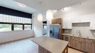 This thoughtfully designed single-floor residence offers a clean, contemporary aesthetic throughout. The open-concept kitchen serves as the heart of the space, featuring a combination of white upper cabinetry and warm wood-toned lower cabinets, complemented by light quartz countertops and a subway tile backsplash. A central island with pendant globe lighting provides additional prep space and serves as a natural focal point. Stainless steel appliances, including a French door refrigerator, dishwasher, microwave, and electric range, complete the functional and stylish kitchen. Light wood-tone luxury vinyl plank flooring runs throughout, tying each area together seamlessly. The living area is open and bright, flowing naturally from the kitchen. The bedroom offers a peaceful retreat with large windows dressed in blackout roller shades, allowing views of the surrounding greenery and outdoor spaces. A well-sized closet with wire shelving provides ample storage. The full bathroom is finished with a warm wood vanity, quartz countertop, an illuminated rectangular mirror, and a full soaking tub with tiled surround. Accessibility features, including a grab bar, are also present. Track lighting and thoughtful fixture choices throughout add to the modern and welcoming character of this residence.