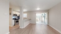 This single-story residence offers a clean, modern aesthetic throughout, unified by light-toned luxury vinyl plank flooring and a neutral gray-and-white color palette. The open-concept layout connects the kitchen directly to the living and dining area, creating a seamless flow ideal for everyday living and entertaining. The kitchen is well-equipped with stainless steel appliances — including a gas range, over-the-range microwave, refrigerator, and dishwasher — complemented by white shaker-style cabinetry, gray quartz countertops, and a single-basin undermount sink. A peninsula with a breakfast bar provides additional counter space and casual seating. The living area is bright and open, drawing natural light through a large sliding glass door that leads to a private outdoor patio. The entry area features a ceiling fan and direct access via a front door with a window. The bedrooms are generously sized, each outfitted with ceiling fans, vertical-blind windows offering views of surrounding greenery, and closet access. The bathroom is tastefully updated with a white shaker vanity, quartz countertop, a framed mirror, and a tiled tub-surround with a built-in niche, maintaining the home's cohesive modern style throughout.