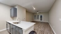This contemporary 680 square foot apartment offers a harmonious blend of style and functionality. The open-concept design seamlessly integrates the living room and kitchen, creating an inviting space for relaxation and entertainment. The kitchen is a standout feature, boasting sleek gray cabinetry, stainless steel appliances, and a convenient breakfast bar.

The bedroom, measuring 160 square feet, provides a cozy retreat with large windows allowing for plenty of natural light. The apartment's neutral color palette, dominated by soft beige walls, creates a calming atmosphere throughout. Wood-look flooring adds warmth and durability to the space.

A private balcony accessible through French doors in the living area extends the living space outdoors, perfect for enjoying fresh air or morning coffee. The apartment also includes a closet for ample storage.

Ceiling fans in the main living areas ensure comfort, while the abundance of windows fitted with blinds offers both natural light and privacy control. The bathroom, though not pictured, likely continues the modern aesthetic found throughout the apartment.

Located in The Quarters at Towson Town Center in Parkville, Maryland, this one-bedroom apartment combines contemporary design with practical living, ideal for those seeking a stylish and efficient living space.