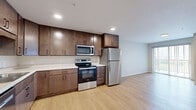 This 1-bedroom, 1-bathroom unit at 505 Malcolm Ave SE in Minneapolis, Minnesota offers a thoughtfully designed layout with modern finishes throughout. Light hardwood flooring runs continuously across the main living areas, creating a bright and cohesive feel.

The open-concept kitchen and living room form the heart of the unit. The kitchen is well-appointed with rich, dark-stained wood cabinetry offering generous upper and lower storage, light countertops, and a full suite of stainless steel appliances including a refrigerator, electric range, over-the-range microwave, and dishwasher. Recessed lighting illuminates the kitchen area, while a sliding glass door in the living space invites natural light and outdoor views.

The bedroom is comfortably sized, featuring light-filled windows with exterior views, light hardwood flooring, and neutral gray walls. A set of wide sliding double closet doors provides ample storage. Additional storage is available through two dedicated closets and a utility room elsewhere in the unit.

The overall aesthetic is clean and contemporary, with a neutral color palette of whites and grays complemented by warm wood tones. The layout is efficient and functional, making excellent use of the available space for comfortable everyday living in a residential Minneapolis setting.