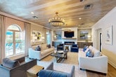Located at 10720 Linkwood Ct in Baton Rouge, LA, this elegantly designed single-floor community space blends modern sophistication with warm, transitional styling throughout. The welcoming reception area anchors the entrance, featuring a reclaimed wood desk beneath a coffered tray ceiling accented by rustic wood beams and a statement chandelier. Large black-framed windows flood the space with natural light and offer views of the outdoor pool area.

The expansive lounge is a standout, boasting a striking herringbone wood-paneled ceiling, a grand candle-style chandelier, and a sleek linear fireplace framed by white brick and a reclaimed wood mantel. Built-in cabinetry in a muted blue-grey finish with gold hardware lines the walls, complemented by coastal-inspired artwork and plush, navy and cream seating arrangements.

A glass-partitioned dining area with bold black steel frames provides a sophisticated visual connection to the adjacent kitchen. The kitchen is outfitted with floor-to-ceiling white shaker cabinetry, gold hardware, a geometric tile backsplash, and a generous marble-topped island. A dedicated workspace features a marble-surfaced conference table and built-in desk area. Light hardwood flooring flows consistently throughout, unifying each area into one cohesive, polished environment.