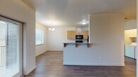 This single-floor residence offers a thoughtfully designed open-concept layout that seamlessly connects the kitchen, dining, and living areas. The kitchen is a standout feature, lined with warm-toned wood cabinetry, granite-style countertops, and a full suite of black appliances including a range, microwave, refrigerator, and dishwasher. A peninsula with bar seating serves as a natural divider between the kitchen and the adjoining dining area, which is accented by an elegant chandelier and a window that brings in natural light. Wood-look plank flooring extends throughout the main living and kitchen areas, adding warmth and visual continuity. A dedicated in-unit laundry area with washer and dryer hookups is conveniently accessible from the kitchen. The bedrooms are carpeted for comfort, with ample natural light provided by windows fitted with blinds. One bedroom features a ceiling fan with a light fixture. The bathrooms are finished with granite-topped wood vanities and tile flooring; one includes a walk-in shower, while another offers a more open layout. Neutral wall tones and clean lines throughout contribute to a bright, move-in-ready ambiance suited for a variety of lifestyles.