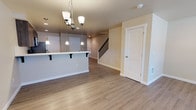 Located at 505 Greenwood Dr SW in Olympia, Washington, this two-floor home offers a well-designed layout with contemporary finishes throughout. The main level features durable light wood-tone luxury vinyl plank flooring that flows seamlessly through the open living and dining areas. A chandelier anchors the dining space, while recessed lighting adds a clean, modern touch. Natural light enters through windows near the entryway, which features a welcoming yellow-accented front door. The kitchen is a functional highlight, equipped with dark wood cabinetry extending to the ceiling, light quartz countertops, a white subway tile backsplash, a stainless steel appliance suite including a refrigerator, electric range with microwave above, and a double-basin sink. A breakfast bar with pendant lighting connects the kitchen to the living area. A staircase with black metal balusters leads to the upper level, where plush neutral carpet runs through the bedrooms. The bedrooms are generously sized, with several offering walk-in closets and natural light from large windows with views of surrounding greenery. The primary bedroom includes an en-suite access door and a wall-mounted heating unit. Clean white trim, neutral warm-toned walls, and consistent finishes throughout give the entire home a cohesive and move-in-ready feel.