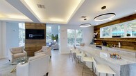 This single-floor clubhouse in Diamond offers a beautifully curated space that seamlessly blends contemporary design with warm, rustic elements. The open-concept layout is anchored by striking reclaimed wood columns and exposed ceiling beams that contrast handsomely against crisp white walls and ceilings, creating a welcoming yet sophisticated atmosphere throughout.

The main gathering area features a generous bar counter finished in luxurious marble-look stone, lined with sleek white bar stools and framed by a reclaimed wood accent wall fitted with display shelving. Overhead, modern circular pendant lights provide a refined focal point, while a tray ceiling with integrated ambient lighting adds depth and warmth to the space.

A comfortable lounge area outfitted with plush neutral-toned armchairs provides an inviting setting for relaxation or socializing, complemented by a large flat-screen television mounted on a matching wood feature wall. Light-toned tile flooring flows continuously throughout, enhancing the sense of openness and cohesion.

Large windows on multiple walls flood the interior with natural light and offer views of the lush outdoor surroundings and pool area beyond the glass entry doors. The overall ambiance is airy, polished, and thoughtfully designed to encourage community and leisure.