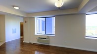 Located at 141 S Harrison St in East Orange, NJ, this single-floor space offers a clean and functional layout with a straightforward, practical design. The main living area is finished with rich hardwood flooring that adds warmth and character throughout the space. A large sliding-style window allows natural light to fill the room, creating a bright and open atmosphere. Beneath the window sits a wall-mounted PTAC heating and cooling unit, providing convenient climate control year-round. The walls are finished in a neutral beige tone, offering a versatile backdrop for a variety of interior styles. A ceiling-mounted light fixture provides overhead illumination, complementing the natural light from the window. The clean lines and open layout of the main area give the space a simple, utilitarian feel. A doorway visible to the side suggests additional rooms or areas beyond the main living space. Overall, the unit presents a well-maintained interior with functional finishes suited for everyday living in the East Orange area.