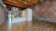Located at 401 S Second St in Leavenworth, Kansas, this single-floor loft-style space showcases a compelling blend of historic industrial character and contemporary updates. Exposed red brick walls run throughout the unit, complemented by striking timber beam ceilings that lend warmth and authenticity to the open living area. Durable wood-look flooring anchors the main living space, which flows seamlessly into a well-appointed kitchen featuring dark wood cabinetry, stainless steel appliances including a refrigerator, range, and over-the-range microwave, and ample counter space. A historic barn-style sliding door adds a standout architectural detail, reinforcing the building's industrial heritage. The bedrooms are carpeted for comfort and each includes sliding closet doors, with exposed brick visible at the upper walls, maintaining the loft aesthetic throughout. Two bathrooms offer modern finishes, including large-format tile surrounds — one with a walk-in shower and grab bar, and another with a full soaking tub and shower combination. Exposed ductwork and conduit add to the industrial character of the space. Natural light enters through multi-pane windows, illuminating the interplay of original and updated materials that define this distinctive Leavenworth address.