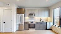 Located in Philadelphia's vibrant North Howard Street corridor, this modern studio unit offers a well-designed, efficiently laid-out single-floor living space. The open-concept main area features light hardwood flooring throughout and a large picture window that fills the room with natural light and frames views of the surrounding neighborhood skyline.

The kitchen is outfitted with a full suite of stainless steel GE appliances, including a French door refrigerator, electric range, over-the-range microwave, and dishwasher. Flat-front cabinetry in a warm wood-tone and soft gray palette extends floor to ceiling, maximizing storage, while a clean tile backsplash and light quartz countertops complete the contemporary aesthetic.

A hallway connects the living area to two closets, providing ample storage. The full bathroom is finished to a high standard, featuring large-format gray porcelain tile flooring, a glass-enclosed walk-in shower with matching tile surround, a wall-mounted LED-backlit mirror, a floating dark wood vanity with white quartz countertop, and matte black hardware accents throughout. Recessed lighting is present throughout the unit, reinforcing the clean, modern feel of this thoughtfully designed Philadelphia residence.