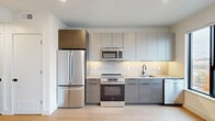 Located in Philadelphia's vibrant North Howard Street corridor, this modern studio unit offers a well-designed, efficiently laid-out single-floor living space. The open-concept main area features light hardwood flooring throughout and a large picture window that fills the room with natural light and frames views of the surrounding neighborhood skyline.

The kitchen is outfitted with a full suite of stainless steel GE appliances, including a French door refrigerator, electric range, over-the-range microwave, and dishwasher. Flat-front cabinetry in a warm wood-tone and soft gray palette extends floor to ceiling, maximizing storage, while a clean tile backsplash and light quartz countertops complete the contemporary aesthetic.

A hallway connects the living area to two closets, providing ample storage. The full bathroom is finished to a high standard, featuring large-format gray porcelain tile flooring, a glass-enclosed walk-in shower with matching tile surround, a wall-mounted LED-backlit mirror, a floating dark wood vanity with white quartz countertop, and matte black hardware accents throughout. Recessed lighting is present throughout the unit, reinforcing the clean, modern feel of this thoughtfully designed Philadelphia residence.