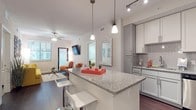 This single-floor residence offers a thoughtfully designed open-concept layout that seamlessly connects the kitchen, dining, and living areas. The kitchen is a standout feature, showcasing granite countertops, a large center island with bar seating, white and gray shaker-style cabinetry, a subway tile backsplash, and a full suite of stainless steel appliances. Pendant and track lighting illuminate the space with a contemporary flair. Rich, dark hardwood-style flooring flows throughout the main living areas, adding warmth and contrast to the light-toned walls and cabinetry. The living room is bright and welcoming, with natural light pouring in through large windows, a ceiling fan, and direct access to an exterior door. The space comfortably accommodates a full seating arrangement. The residence includes two bedrooms, each with plush carpet, ceiling fans, and ample natural light. One bedroom features an ensuite bathroom, while both bathrooms are finished with granite-topped vanities, gray cabinetry, framed mirrors, and light tile flooring. One bathroom includes a tub-shower combination, while the other offers a separate shower. A walk-in closet provides generous storage. The overall ambiance is modern, clean, and cohesive throughout.