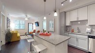This single-floor residence offers a thoughtfully designed open-concept layout that seamlessly connects the kitchen, dining, and living areas. The kitchen is a standout feature, showcasing granite countertops, a large center island with bar seating, white and gray shaker-style cabinetry, a subway tile backsplash, and a full suite of stainless steel appliances. Pendant and track lighting illuminate the space with a contemporary flair. Rich, dark hardwood-style flooring flows throughout the main living areas, adding warmth and contrast to the light-toned walls and cabinetry. The living room is bright and welcoming, with natural light pouring in through large windows, a ceiling fan, and direct access to an exterior door. The space comfortably accommodates a full seating arrangement. The residence includes two bedrooms, each with plush carpet, ceiling fans, and ample natural light. One bedroom features an ensuite bathroom, while both bathrooms are finished with granite-topped vanities, gray cabinetry, framed mirrors, and light tile flooring. One bathroom includes a tub-shower combination, while the other offers a separate shower. A walk-in closet provides generous storage. The overall ambiance is modern, clean, and cohesive throughout.