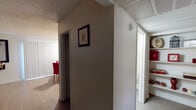 This single-floor residence offers a comfortable and functional layout across several distinct living areas. The expansive living room is a standout feature, providing generous space for seating and relaxation, with light wood-tone flooring, a textured ceiling, and neutral walls that create a warm, inviting atmosphere. A large wall-mounted mirror adds depth to the room.

The kitchen is well-equipped with warm wood cabinetry extending to the ceiling, ample countertop space, a stainless steel sink, and white appliances including a range and refrigerator. An adjoining utility area conveniently houses a full-size washer and dryer alongside additional kitchen appliances, with a window providing natural light.

The primary bedroom features plush carpeting, a window with drape treatments, and generous closet space. A second bedroom, also carpeted, comfortably accommodates multiple beds and includes its own window with vertical blinds. A central hallway connects the rooms, featuring a textured ceiling and access to built-in shelving.

The bathroom is clean and functional, featuring a wood-toned vanity with a large mirror and a bright vanity light, a stand-alone shower stall, and light wood-look flooring. Throughout the space, a consistent neutral color palette and textured ceilings unify the overall design, creating a cohesive and livable environment.