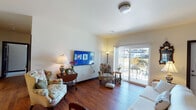 This single-floor residence offers a thoughtfully designed layout with quality finishes and a warm, welcoming ambiance throughout. The heart of the home is a well-equipped kitchen featuring rich dark-stained cabinetry, granite countertops, stainless steel appliances including a refrigerator, microwave, and range, and a peninsula with pendant lighting that provides additional workspace and casual seating. Warm hardwood flooring flows through the kitchen and connects seamlessly to the main living areas.

The living room is bright and inviting, with hardwood floors, a wall-mounted flat-screen television, and a sliding glass door that opens to an outdoor patio, allowing ample natural light to fill the space. A secondary sitting room offers plush carpeting, a large window with neighborhood views, and a relaxed atmosphere ideal for reading or conversation.

The bedroom is generously sized with soft carpeting, a window that invites natural light, and a calm, restful feel. Two full bathrooms serve the residence, each featuring dark cabinetry, granite vanity countertops, and hardwood-style flooring. One bathroom includes a tub-shower combination, while the other offers a walk-in shower setup with additional storage. Together, these spaces create a comfortable and cohesive home environment.