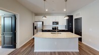 Located at 15927 White St in Charlotte, NC, this single-story home offers a thoughtfully designed open-concept layout with contemporary finishes throughout. The living area features warm wood-look flooring, recessed lighting, and pendant lights that create an inviting atmosphere. Large windows fitted with blinds allow generous natural light to fill the space, while a glass-paneled entry door enhances connectivity to the outdoors.

The kitchen serves as a central hub of the home, anchored by a substantial granite-topped island with an undermount sink and seating overhang. White shaker-style upper cabinets contrast elegantly with dark lower cabinetry, complemented by a subway tile backsplash and a full suite of stainless steel appliances, including a refrigerator with ice maker, electric range, and built-in microwave.

The bedrooms are carpeted for comfort, each featuring ceiling fans and ample natural light through blinds-equipped windows. Two bathrooms reflect the same design cohesion found throughout the home, featuring dark vanity cabinetry, granite countertops, large framed mirrors, and wood-look flooring. The primary bathroom includes a double-sink vanity, while the secondary bath offers a tub-shower combination with tiled surround.