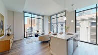 Located in the heart of downtown Cincinnati at 407 Race St, this modern urban residence offers a thoughtfully designed open-concept layout flooded with natural light. Dramatic floor-to-ceiling windows with sleek black frames define the living and dining area, framing panoramic views of the Cincinnati skyline and creating a seamless connection between interior and city.

The kitchen is well-appointed with warm wood cabinetry, stainless steel appliances including a range, over-the-range microwave, and refrigerator, complemented by white quartz countertops, a subway tile backsplash, and light hardwood-style flooring. A peninsula with an undermount sink provides additional prep space and casual seating.

Two bedrooms each benefit from expansive floor-to-ceiling windows with striking urban vistas. The primary bedroom is served by an en-suite bathroom featuring a glass-enclosed shower, large-format tile flooring, and a vanity with quartz countertops. A second full bathroom includes a soaking tub with tiled surround. A dedicated in-unit laundry closet with full-size washer and dryer adds everyday convenience. Clean lines, neutral tones, and contemporary finishes throughout create a cohesive, modern ambiance ideal for urban living.