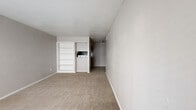 Located at 6233 Gulfton St in Houston, TX, this single-floor unit offers two bedrooms and one bathroom within a compact, efficiently arranged floor plan. The living area features plush carpet flooring, a large window dressed with horizontal blinds that allows natural light to fill the room, and a textured ceiling. Built-in open shelving along one wall provides practical storage, while a pass-through opening offers a direct sightline into the kitchen area, which is equipped with standard appliances including a range. The primary bedroom is generously proportioned, featuring soft carpet flooring, a ceiling fan with light fixture, and a window with blinds that brings in additional natural light. A closet with a standard door adds convenient storage to the room. The second bedroom mirrors a similar layout with carpet flooring and a ceiling fan. The bathroom includes a toilet, a shower-tub combination, and a countertop vanity area. Neutral gray and beige tones are carried throughout the unit, lending a clean and cohesive aesthetic. The tile flooring in the kitchen and bathroom provides a practical contrast to the carpeted living and sleeping areas. Overall, the space presents a straightforward, functional layout suited for everyday living.