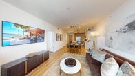 This thoughtfully designed single-floor residence showcases a seamless blend of contemporary style and functional living. The open-concept layout connects the kitchen, dining, and living areas into one cohesive, light-filled space. The kitchen is outfitted with white flat-panel upper cabinetry, warm wood lower cabinets, a marble-look quartz backsplash and countertops, stainless steel appliances, and a central island with bar seating — ideal for both casual dining and entertaining. Light wood-toned flooring flows consistently throughout the main living areas, enhancing the sense of continuity and warmth. The living room benefits from floor-to-ceiling windows and direct access to an outdoor balcony, offering sweeping exterior views and abundant natural light. Two bedrooms provide restful retreats, each finished in neutral tones and accented with curated artwork. One bedroom features a ceiling fan and city-facing window, while both are furnished with upholstered headboards and refined gold-accented nightstands. The two bathrooms are finished in a crisp, spa-like aesthetic, featuring marble-style tile flooring, wood-toned vanities with white countertops, and illuminated mirrors. One bathroom includes a glass-enclosed walk-in shower, while the other offers a combined shower and tub. Track lighting throughout the home adds a modern, polished touch to every room.