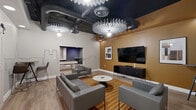 Located at 2901 Connecticut Ave NW in Washington, DC, this contemporary lounge space offers a thoughtfully designed communal retreat with a distinct urban personality. The single-floor layout is anchored by an open living area furnished with modern gray sofas, accent chairs, and a sleek marble-top coffee table, all arranged atop a bold striped area rug over warm wood-look flooring.

A standout design feature is the large-scale Washington, DC skyline mural rendered in minimalist black linework across the neutral walls, lending the space a strong sense of place and artistic character. An accent wall in a rich golden-ochre hue adds warmth and contrast, complemented by framed artwork and a wall-mounted flat-screen television above a low-profile media console.

The exposed black ceiling reveals industrial ductwork and is punctuated by striking fan-shaped decorative light fixtures that serve as sculptural focal points while providing ambient illumination. Recessed lighting adds further brightness throughout.

A set of white sliding barn doors opens to an adjacent room visible in the background, featuring a pool table and dining-height seating, hinting at additional recreational amenities. The overall ambiance is modern, inviting, and creatively curated — making this lounge an engaging social hub in the heart of Washington, DC.