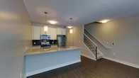 This two-story home showcases a thoughtfully designed open-concept main level where the kitchen serves as a central focal point. The kitchen is outfitted with stainless steel appliances, including a range, microwave, and refrigerator, complemented by crisp white cabinetry that extends to the ceiling. A dark mosaic tile backsplash adds a striking contrast against the light cabinetry, while the granite-topped peninsula provides additional prep space and casual seating. Pendant lighting hangs above the peninsula, contributing to the warm, layered lighting scheme throughout the main level.

Dark hardwood flooring runs continuously across the main floor, grounding the space with a rich, contemporary aesthetic. The open layout allows the kitchen to flow seamlessly into the adjacent living area, creating a cohesive and functional entertaining space. A staircase with a sleek metal baluster railing leads to the upper level, adding an architectural element that enhances the home's modern character. Recessed and flush-mount ceiling fixtures provide consistent illumination throughout, contributing to an inviting and well-lit atmosphere across both levels.