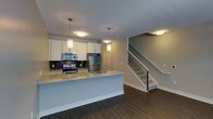 This two-story home showcases a thoughtfully designed open-concept main level where the kitchen serves as a central focal point. The kitchen is outfitted with stainless steel appliances, including a range, microwave, and refrigerator, complemented by crisp white cabinetry that extends to the ceiling. A dark mosaic tile backsplash adds a striking contrast against the light cabinetry, while the granite-topped peninsula provides additional prep space and casual seating. Pendant lighting hangs above the peninsula, contributing to the warm, layered lighting scheme throughout the main level.

Dark hardwood flooring runs continuously across the main floor, grounding the space with a rich, contemporary aesthetic. The open layout allows the kitchen to flow seamlessly into the adjacent living area, creating a cohesive and functional entertaining space. A staircase with a sleek metal baluster railing leads to the upper level, adding an architectural element that enhances the home's modern character. Recessed and flush-mount ceiling fixtures provide consistent illumination throughout, contributing to an inviting and well-lit atmosphere across both levels.