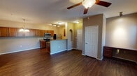 This single-floor residence offers a thoughtfully designed open-concept layout that seamlessly connects the living, dining, and kitchen areas. Rich, dark hardwood-style flooring runs throughout the main living spaces, providing a warm and cohesive aesthetic. Ceiling fans are installed in the living area and bedrooms, contributing to both comfort and style.

The kitchen is a functional highlight, featuring stainless steel appliances including a gas range, microwave, and refrigerator, complemented by warm wood cabinetry and granite-style countertops. A breakfast bar peninsula separates the kitchen from the living area, while a chandelier above adds an elegant touch. Track lighting illuminates the workspace efficiently.

The living area is bright and open, with a built-in desk nook and access to an outdoor balcony or patio through a glass door, allowing natural light to flow freely into the space. The bedrooms are generously sized, each with ceiling fans and large windows dressed with vertical blinds.

The bathrooms are finished with neutral tile flooring, rich wood vanities with granite-style countertops, and large mirrors. One bathroom features a soaking tub with shower combination, while another offers a spacious layout with ample storage. An arched architectural detail near the entryway adds a subtle decorative element to the overall design.