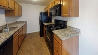 Located at 1 Lilac in Dover, New Hampshire, this single-floor residence offers a practical and comfortable layout designed for everyday living. The kitchen is well-appointed with warm honey-toned cabinetry, granite countertops, tile flooring, and black appliances including a refrigerator, electric range, and over-the-range microwave — providing a functional workspace for cooking and meal preparation. The kitchen flows openly into a generously sized living area, which features plush wall-to-wall carpeting, a textured ceiling, and access to a patio or balcony through a sliding glass door, allowing for natural light to fill the space. Multiple bedrooms are finished with soft carpeting, neutral white walls, and windows fitted with blinds for privacy and light control, offering comfortable and adaptable living spaces. Two full bathrooms echo the kitchen's design aesthetic, each featuring granite-topped wood vanities, tile flooring, and a tub/shower combination. One bathroom includes a built-in linen closet with wire shelving for added storage convenience. Throughout the residence, consistent finishes and a clean, neutral palette create a cohesive and move-in ready environment.