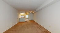 This single-floor residence offers a straightforward, functional layout designed to maximize usable space. The expansive living area is carpeted in warm beige tones and features a ceiling fan, overhead ventilation, and ample wall space, providing a versatile canvas for various furniture arrangements. A ceiling fan overhead adds both comfort and a practical element to the room.

The kitchen is designed in a galley configuration, featuring light wood cabinetry lining both sides, laminate countertops, white appliances including a gas range and refrigerator, a double sink, and a dishwasher. A tiled backsplash adds a clean, finished look to the space. A peninsula counter connects the kitchen to the living area, creating a natural transition between the two spaces.

The bedroom is generously sized with soft carpeting and a large window dressed with horizontal blinds, allowing abundant natural light to filter in while maintaining privacy.

The bathroom features a full tub-and-shower combination with distinctive blue ceramic wall tiles, complemented by wood-look tile flooring. The overall palette throughout the unit is neutral and clean, offering a blank slate well-suited for personalization.