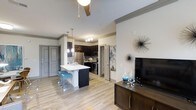 Located at 1570 Atria Cir in Raleigh, NC, this single-floor residence offers a thoughtfully designed open-concept living space that seamlessly connects the kitchen, dining, and living areas. Light hardwood-style flooring runs throughout, contributing to a bright and cohesive aesthetic.

The kitchen is a standout feature, showcasing dark cabinetry that contrasts sharply with a white waterfall-edge island, complete with seating for casual dining. Pendant lighting hangs above the island, complementing the stainless steel appliances, including a refrigerator and range. A mosaic tile backsplash adds a decorative touch behind the cooking area.

The living area is anchored by a ceiling fan overhead and flows naturally from the kitchen, offering a comfortable and functional layout. A media console with a flat-screen TV is positioned against a neutral-toned accent wall adorned with decorative wall art, adding personality to the space.

Crown molding details frame the ceilings, enhancing the overall refined character of the interior. The open layout and neutral color palette create a welcoming ambiance, making the space feel airy and well-appointed throughout.