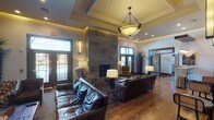 The Crowne at Timberline clubhouse is a single-story amenity space designed with a sophisticated, lodge-inspired aesthetic that balances comfort and functionality. The main lounge serves as the centerpiece, featuring soaring ceilings with cove lighting, a commanding floor-to-ceiling stone fireplace, rich hardwood flooring, and plush leather seating arranged for relaxed gathering. Double French doors invite abundant natural light and outdoor views. A textured reclaimed wood accent wall with a mounted flat-screen television anchors a secondary lounge area, creating a warm, inviting atmosphere.

Adjacent to the lounge is a café-style sitting area outfitted with oversized pendant lighting, upholstered seating, and a beverage station — ideal for casual work or socializing. A compact kitchenette features dark espresso cabinetry, granite-style countertops, stainless steel appliances, and a distinctive backlit log-art wall installation that adds an artistic, nature-inspired focal point.

The fitness center is expansive and well-lit, offering a comprehensive selection of cardio equipment including treadmills and ellipticals, as well as a full circuit of strength training machines branded with the Crowne at Timberline logo. Floor-to-ceiling mirrors, ceiling fans, and large windows enhance the open, airy feel of the workout space.