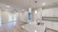 Located at 143 Emerson Point Dr in Elon, NC, this well-appointed 2-bedroom, 2-bathroom single-floor home offers a thoughtfully designed layout with modern finishes throughout. The open-concept living, dining, and kitchen area serves as the heart of the home, anchored by a central kitchen island topped with granite countertops and an undermount sink. White shaker-style cabinetry, stainless steel appliances — including a range, microwave, and refrigerator — and stylish pendant lighting complete the kitchen. Light wood-tone flooring runs throughout the main living areas, lending warmth and continuity to the space. The living room is bright and airy, featuring a ceiling fan and French doors that open to the outdoors, filling the room with natural light. Both bedrooms are carpeted for comfort, with the primary bedroom offering generous proportions and its own closet. The two bathrooms mirror the home's refined aesthetic, each featuring granite-topped vanities with white cabinetry and wood-look flooring. Additional conveniences include a dedicated laundry area, a pantry, and four closets providing ample storage. The entrance corridor leads seamlessly into the main living area, creating a welcoming and functional flow throughout this clean, move-in-ready home.