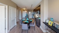 Located at 44 Maryland Ave in Rockville, Maryland, this well-appointed apartment offers a thoughtfully designed single-floor layout with modern finishes and a cohesive aesthetic throughout. The open-concept kitchen is a standout feature, showcasing rich dark cabinetry, granite countertops, a mosaic tile backsplash, and a full suite of stainless steel appliances. Track lighting illuminates the space, while wood-style flooring extends seamlessly into the adjacent dining area, which comfortably accommodates a round table with seating for four beneath stylish pendant lights. The living and dining areas flow together to create an inviting, functional common space. The bedroom is generously proportioned, featuring plush carpeting, access to a walk-in closet, and a large window with sliding glass door that opens to a private balcony with urban views of the Rockville skyline. The bathroom is finished with large-format tile flooring, a granite-topped vanity with dark cabinetry, and a full soaking tub with shower combination. Neutral warm-toned walls throughout the residence create a calm, contemporary ambiance that is both stylish and practical.