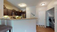 Located at 50 Paces Pkwy in Woodstock, Georgia, this single-floor residence offers a well-designed open-concept layout that seamlessly connects the main living areas. Rich hardwood-style flooring runs throughout the common spaces, complemented by crown molding and soft neutral wall tones that create a cohesive, inviting ambiance.

The living room is generously proportioned, featuring a ceiling fan and natural light from windows overlooking greenery. Decorative columns elegantly define the transition into the dining area, which is accented by a pendant light fixture and offers convenient proximity to both the kitchen and a dedicated laundry closet housing a full-size front-loading washer and dryer.

The kitchen is equipped with dark espresso cabinetry, granite-style countertops, stainless steel appliances including a refrigerator, microwave, and range, and a raised breakfast bar with seating — ideal for casual dining. A separate entry door is also accessible from the kitchen area.

The bedrooms are carpeted for comfort, each featuring ceiling fans and ample space. The bathroom is finished with dark cabinetry, a framed mirror, light countertops, and hardwood-style flooring, offering a clean and functional design.

This single-story residence combines practical amenities with stylish finishes throughout.