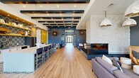 Located at 208 Windfall Way in Myrtle Beach, SC, this generously sized single-floor space delivers a polished coastal-modern aesthetic throughout its open, well-appointed layout. The expansive main lounge serves as the centerpiece, anchored by a dramatic floor-to-ceiling stone fireplace with a sleek three-sided electric insert. Overhead, a mix of exposed dark wood beams, shiplap ceilings, and pendant lighting—ranging from woven rattan fixtures to oversized ceramic dome pendants—creates visual depth and warmth. Light-toned hardwood flooring flows throughout, unifying each area seamlessly.

The kitchen and bar zone features a large white island with bar seating, open wood shelving, bold geometric-patterned tile backsplash and flooring, terrazzo countertops, and a statement driftwood branch accent. Adjacent dining seating adds functional versatility to the area.

A wide central corridor, framed by navy-trimmed glass doors and curated wall art, connects the spaces and leads to French doors that open to an outdoor pool deck, flooding the interior with natural light. Additional seating nooks with armchairs offer inviting spots for casual gathering. The overall ambiance is vibrant yet refined, combining coastal textures with bold color accents of deep teal, gold, and warm wood tones.