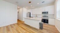 Located at 14520 Avalon Rd in Winter Garden, FL, this single-story, one-bedroom, one-bathroom unit offers a thoughtfully designed layout that maximizes functionality. Light wood-style flooring flows throughout the space, complemented by crisp white walls and recessed lighting that create a clean, modern aesthetic.

The heart of the unit is a combined living, dining, and kitchen area. The kitchen stands out with sleek white cabinetry, granite countertops, a white subway tile backsplash, and a full suite of stainless steel appliances including a French door refrigerator, electric range, and over-the-range microwave. A central island with matching granite provides additional prep space and seating, while a linear pendant light and ceiling fan add stylish overhead illumination. Natural light enters through a window overlooking the space.

A hallway fitted with a sliding barn door connects the main living area to the private spaces. The bedroom is a cozy, well-proportioned room with recessed lighting and a ceiling fan. A dedicated closet and in-unit laundry area add practical convenience.

The bathroom features large-format neutral floor tiles, white cabinetry with black hardware, a granite vanity top, and a walk-in glass-enclosed shower with white tile surround, delivering a polished, spa-like finish.